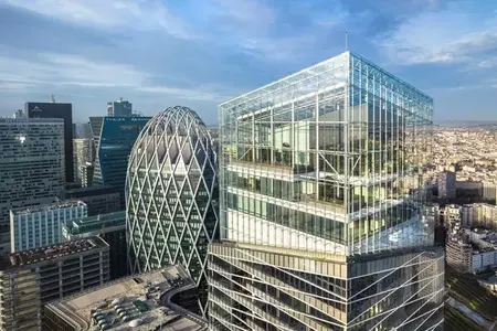 Luchtfoto van moderne hoogbouw in het zakendistrict La Défense in Parijs. Rechts de Saint-Gobain toren, een glazen constructie met zichtbare draagconstructie en terrassen, links een ovaalvormig gebouw met een ruitvormig patroon op de gevel. Op de achtergrond een uitgestrekt stedelijk landschap.